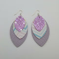Pair of earrings with purple glittery center and multicolored outer layer on a light purple surface