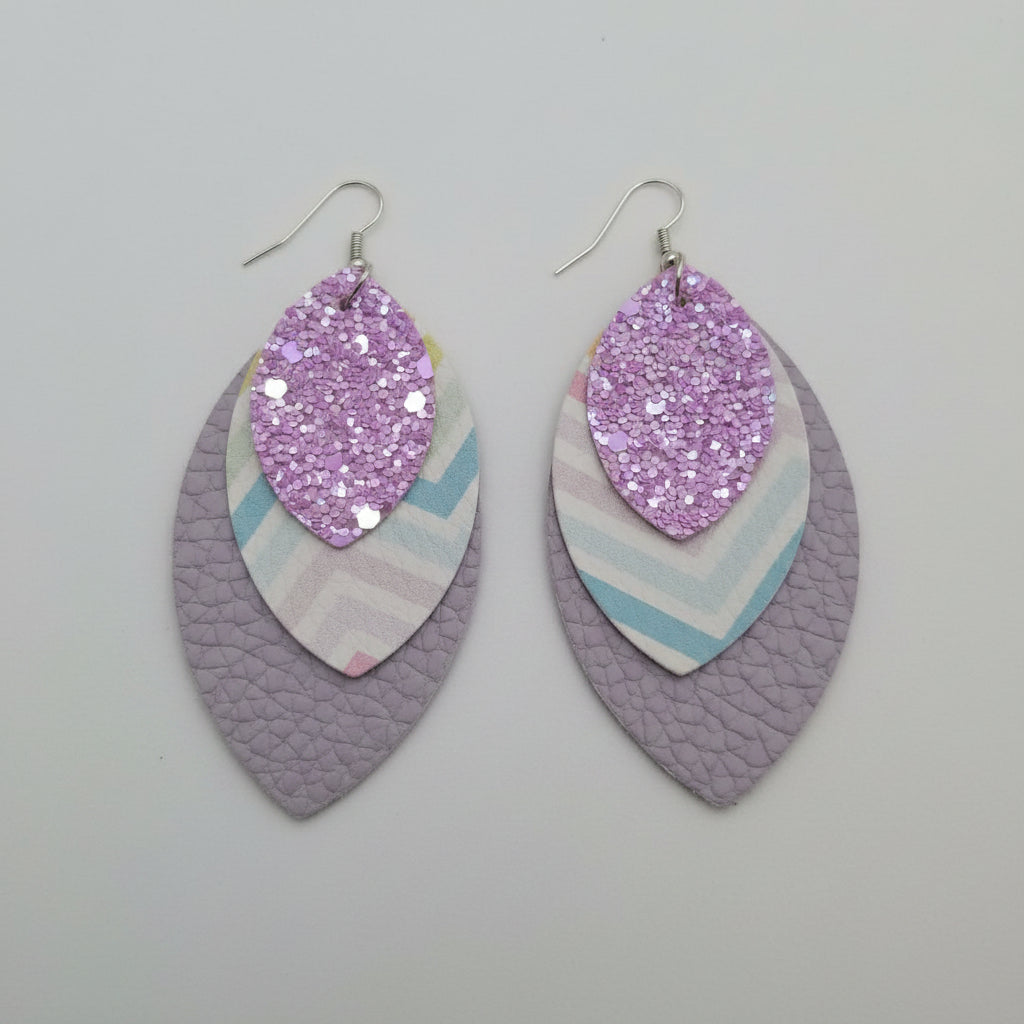 Pair of earrings with purple glittery center and multicolored outer layer on a light purple surface