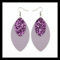 Purple glittery leaf-shaped earrings on gray textured surface